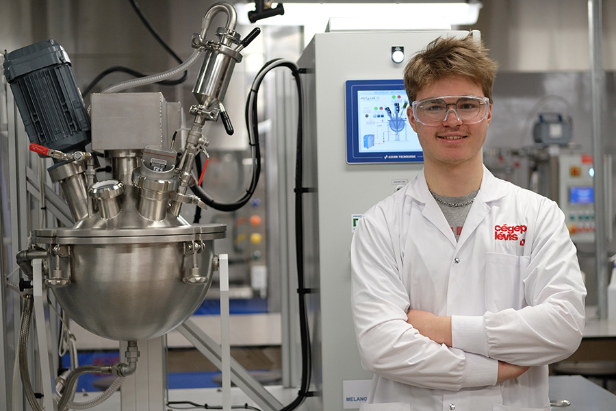 Étudiant portant un sarrau du Cégep de Lévis devant des équipements de production.